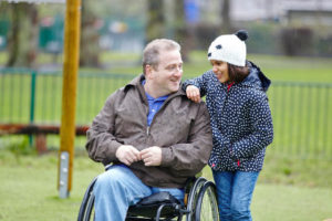 Male carer wheel chair user and young female child in the park